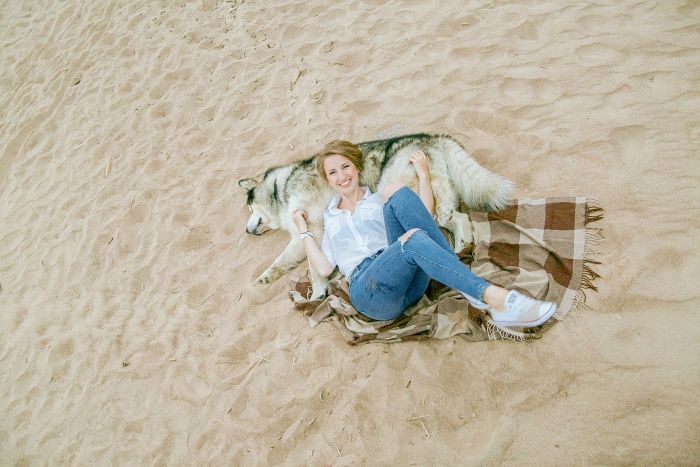 Kobieta leży przy psie na plaży.